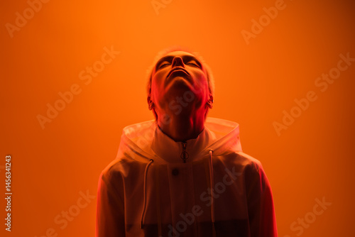 A person wearing a hoodie looks upwards, backlit in warm orange lighting. The image conveys a sense of emotion, introspection, and artistic expression, merging vibrant warm tones and dramatic