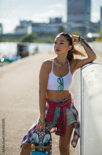 Foto Mulatto girl walks along the embankment with a skateboard and a volleyball, a mu