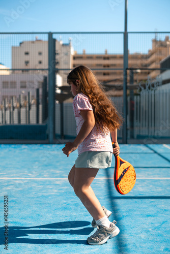 Girl playing paddle tennis on a sunny urban court.