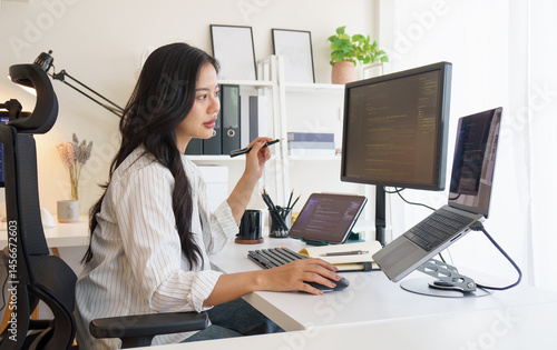 Software developer working on coding project with multiple monitors in modern home office..