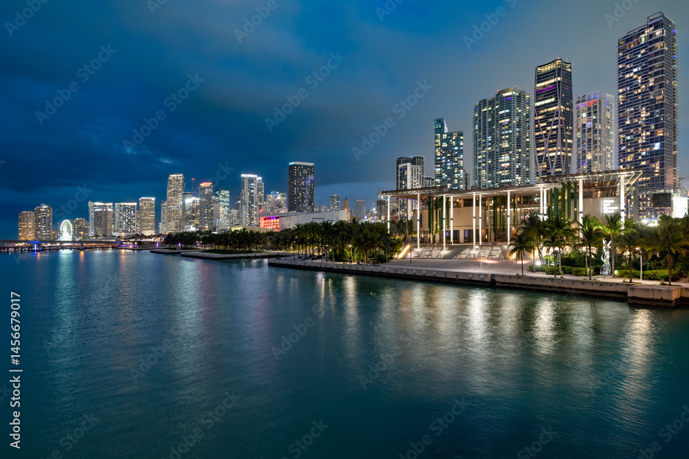 Fototapeta premium Panoramic view of modern skyscrapers glowing at dusk alongside the waterfront Maurice A. Ferré Park in downtown Miami.