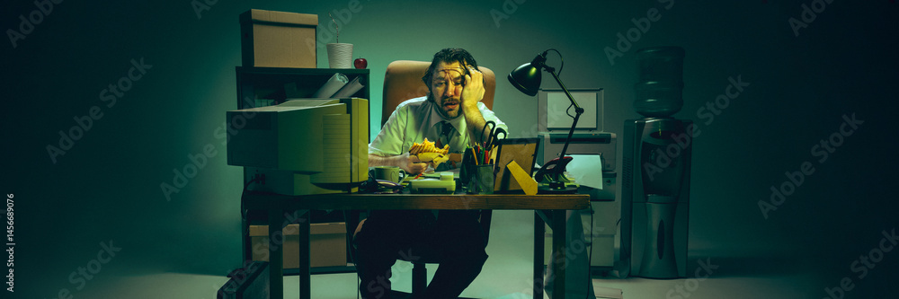 Frustrated man rests head on hand, holding sandwich at desk buried in files, expressing burnout, corporate pressure, stress and multitasking. Concept of retro office, corporate life, overwork