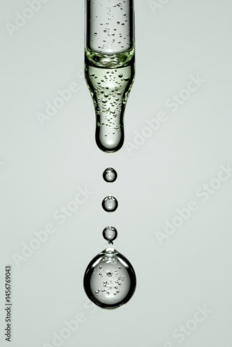 Obraz na płótnie Clear liquid drops fall from a glass dropper, suspended in mid-air with visible air bubbles inside. w salonie