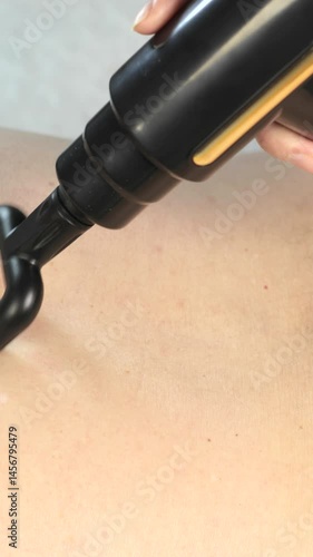 Vertical video of physiotherapy and rehabilitation after intervertebral hernia on spine. Massage on man's back with percussion massage gun. Close up, 4k footage.