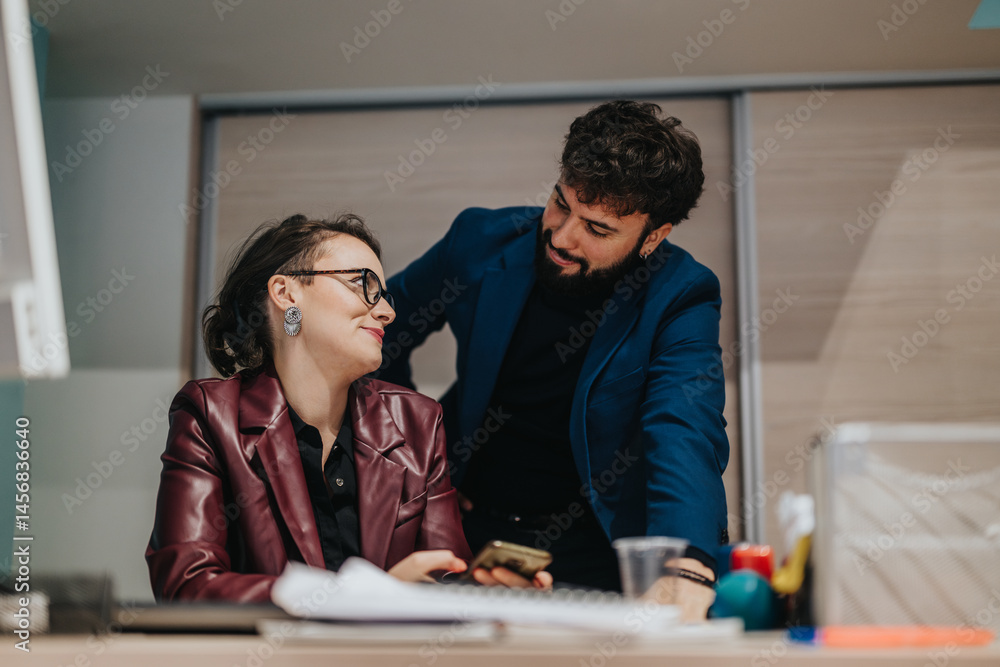 Fototapeta premium Two professional colleagues are engaged in discussion at a modern office setting, showcasing collaboration and teamwork. The interaction highlights a productive and friendly corporate atmosphere.