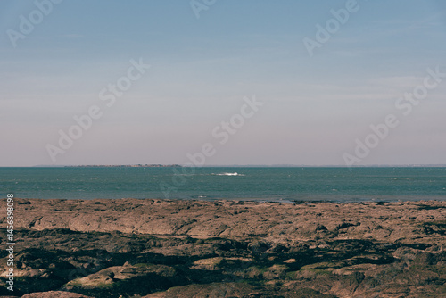 A wide view of the open ocean from a rocky shore, with distant waves and clear skies