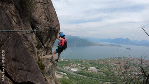 Via Ferrata Picasass, Baveno, Lake Maggiore - Hooked to the cliffside, a woman climber ascends the vertical slab, Lake Maggiore’s horizon blurring behind distant haze and steel rungs.