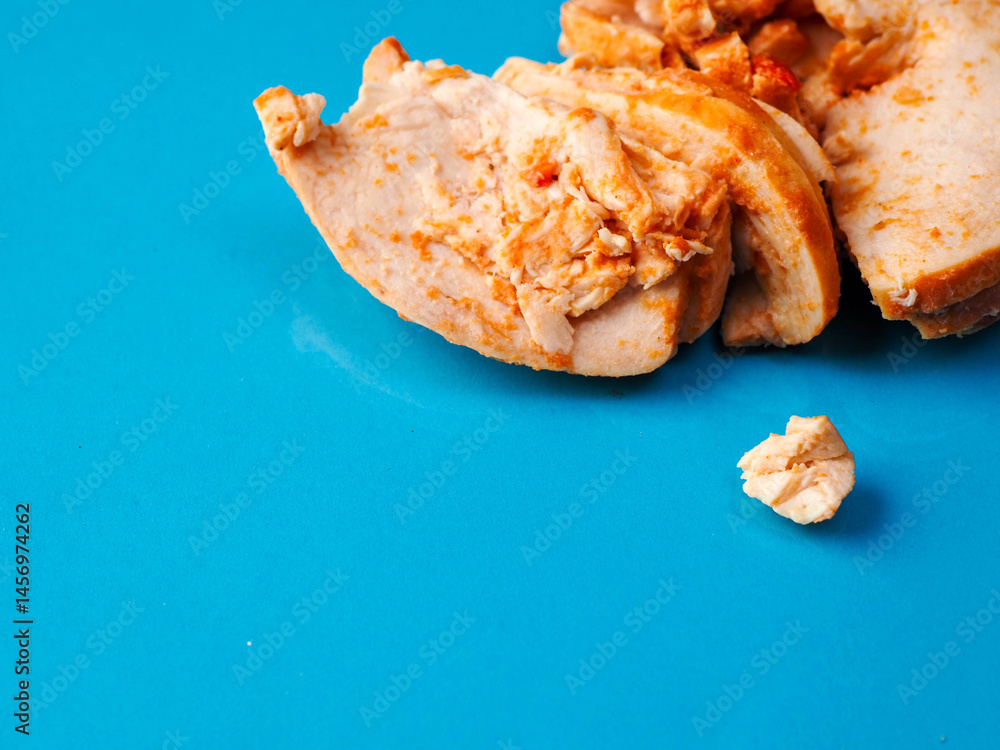 A tray of Cajun style chicken is on a blue background. The chicken is cut into pieces. Small portion of poultry meat, ready to be eat or used for a sandwich.