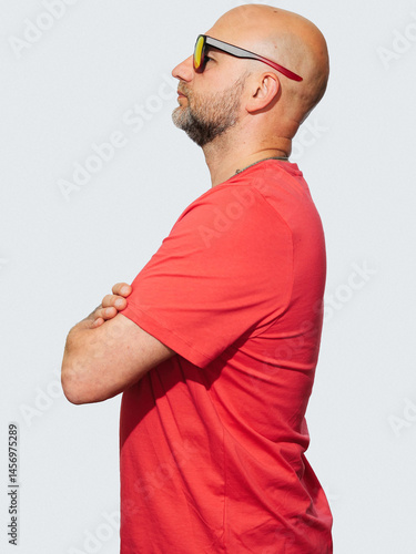 Obraz na płótnie A man in a red shirt is standing with his arms crossed. He has a serious expression on his face, light color background. Male in his 40s with grey beard and bold head, slim body type. w salonie