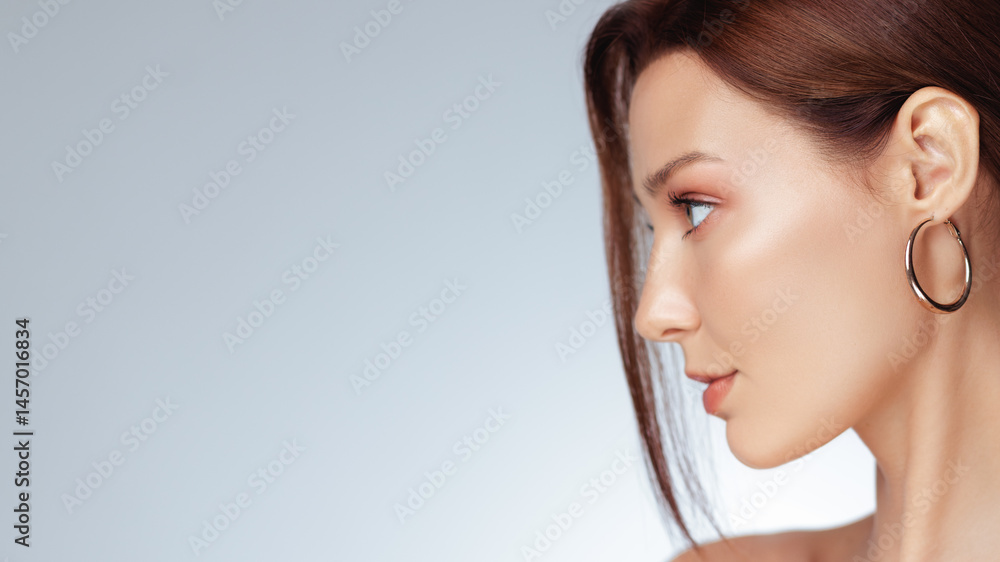 Minimalist fashion banner showing a woman in profile with smooth glowing skin, soft makeup, and a statement gold hoop earring. Perfect for high-end beauty or skincare ads.