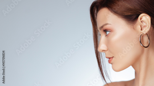 Obraz na płótnie Minimalist fashion banner showing a woman in profile with smooth glowing skin, soft makeup, and a statement gold hoop earring. Perfect for high-end beauty or skincare ads. w salonie