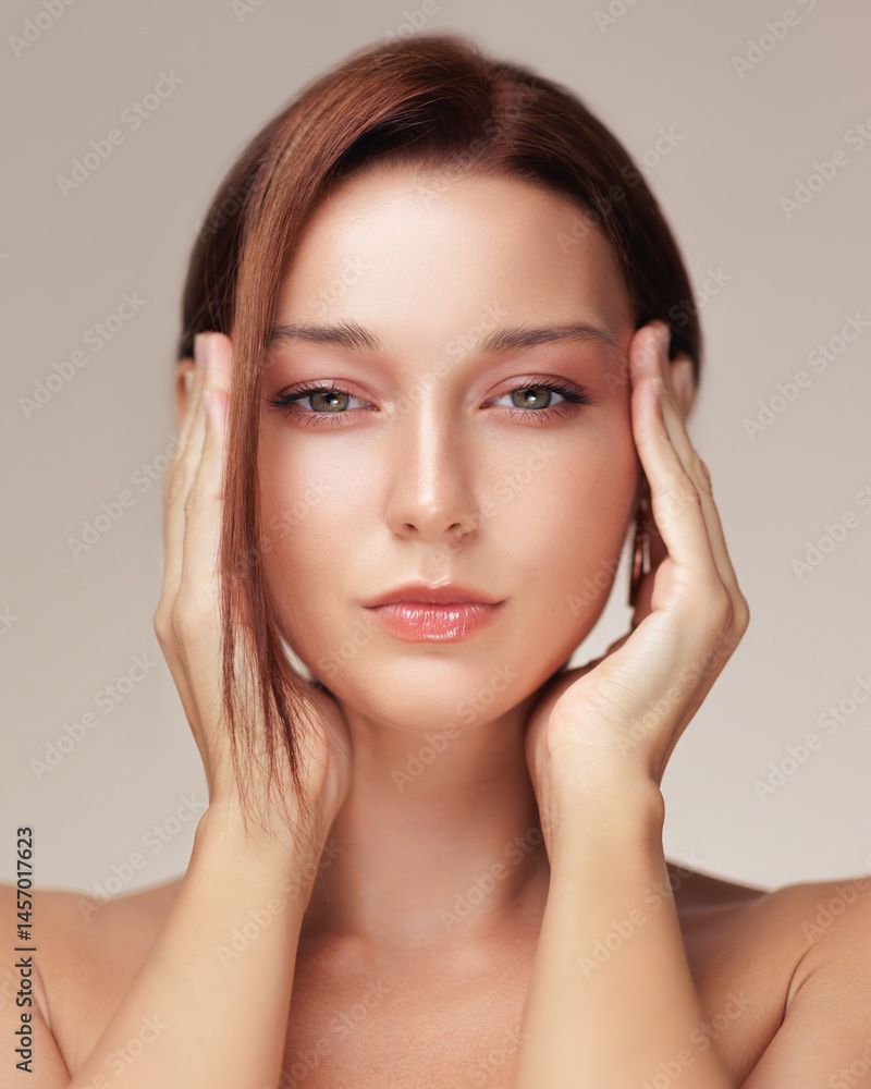 Closeup of a young woman with glowing skin and glossy lips pressing her hands to her face, evoking facelift or eye lift effects - ideal for skincare, anti-aging, or cosmetic product campaigns.