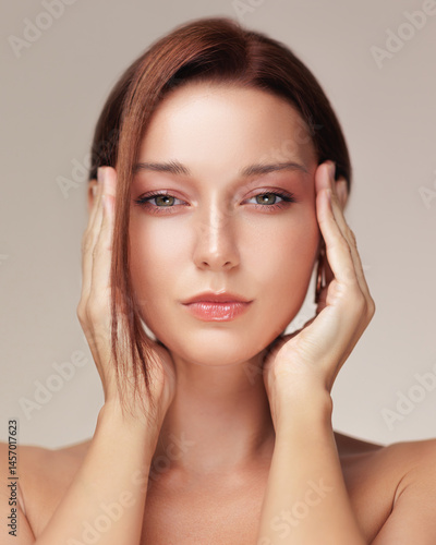 Closeup of a young woman with glowing skin and glossy lips pressing her hands to her face, evoking facelift or eye lift effects - ideal for skincare, anti-aging, or cosmetic product campaigns.