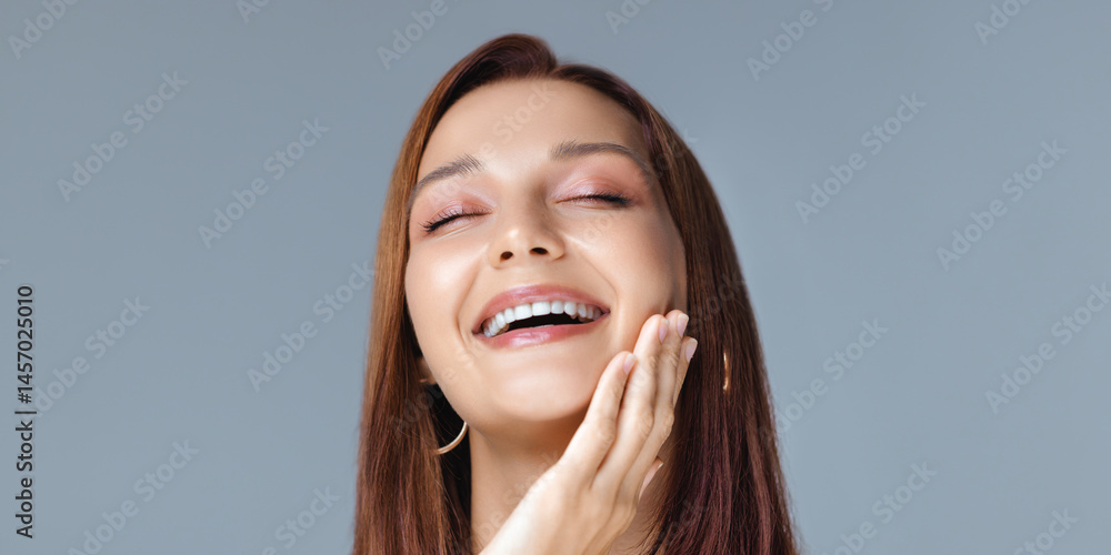 Charming young woman with smooth glowing skin, glossy lips, and hoop earrings laughing with joy in a studio setting - perfect for skincare, beauty, or self-care advertisement visuals.