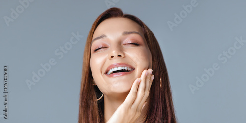 Obraz na płótnie Charming young woman with smooth glowing skin, glossy lips, and hoop earrings laughing with joy in a studio setting - perfect for skincare, beauty, or self-care advertisement visuals. w salonie