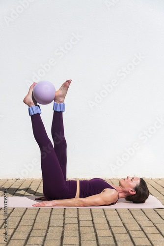 fit woman doing pilates exercises with a ball, legs raised