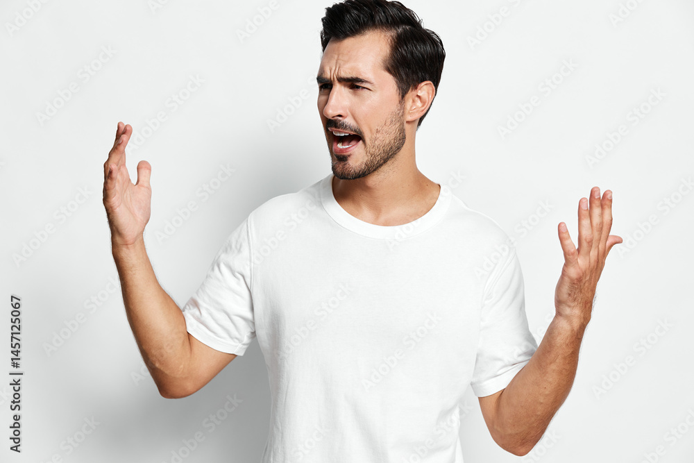 Expressive man gesturing with hands in frustration, wearing a casual white t-shirt, against a light grey background. Emotion and communication concept. Expressive man gesturing with hands in frustration, wearing a casual white t-shirt, against a light grey background. Emotion and communication concept.
