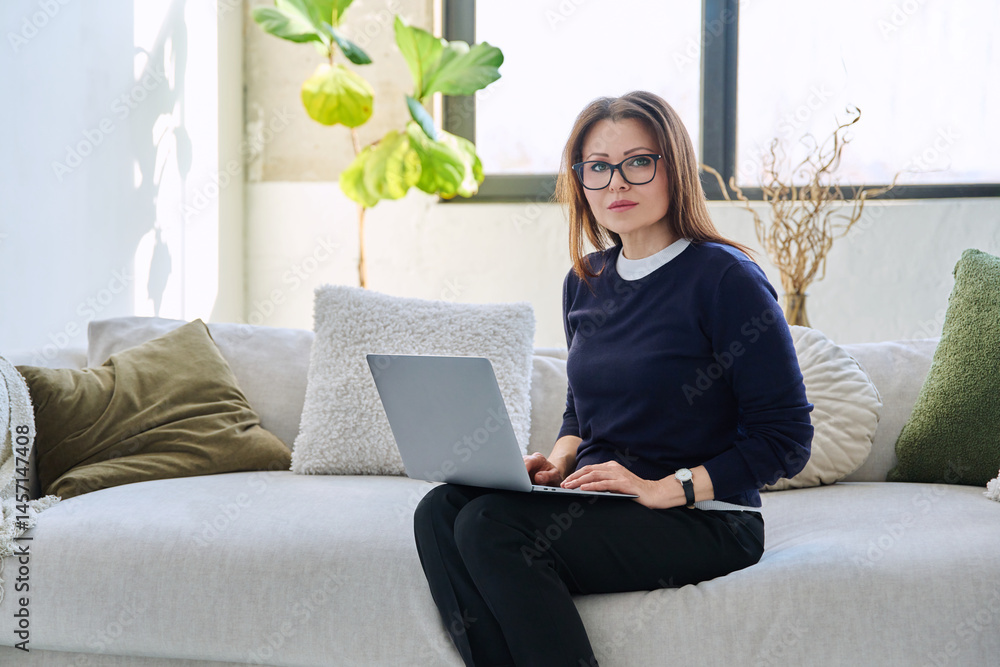 Portrait of middle aged woman with laptop sitting on sofa at home