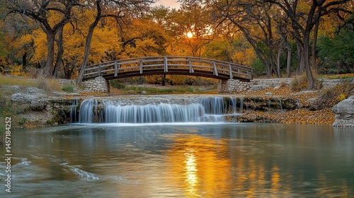 Fototapeta Naklejka Na Ścianę i Meble -  Autumnal waterfall and wooden bridge over calm creek. Golden fall colors paint trees around tranquil water