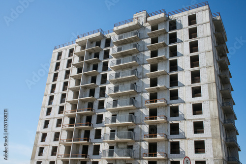 large grey brick multi-storey building under construction against a clear blue sky