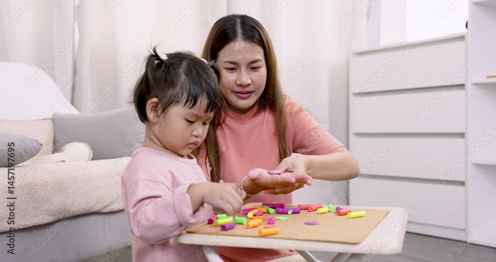 Asian single mother attentively teaches preschool daughter to mold clay, guiding small hands, encouraging exploration, bonding through playful learning, warm supportive interaction in cozy home. Asian single mother attentively teaches preschool daughter to mold clay, guiding small hands, encouraging exploration, bonding through playful learning, warm supportive interaction in cozy home.