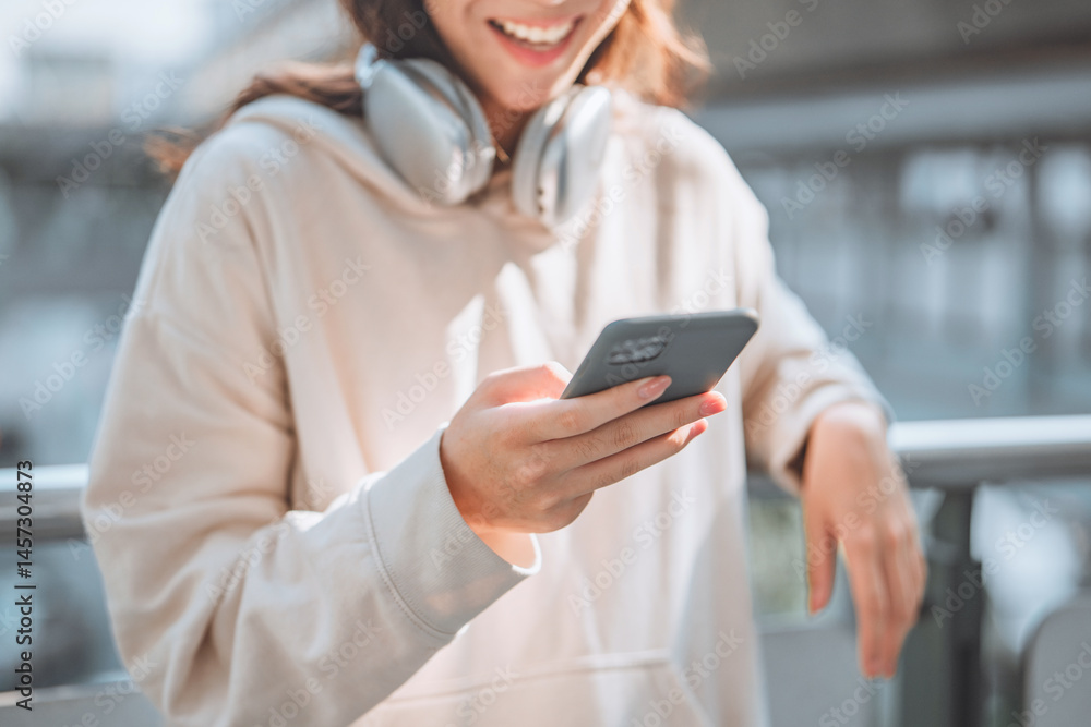 Fototapeta premium Close-up of happy asian teenage girl wearing headphones using smartphone in urban city – enjoying social media, online communication and digital lifestyle concept