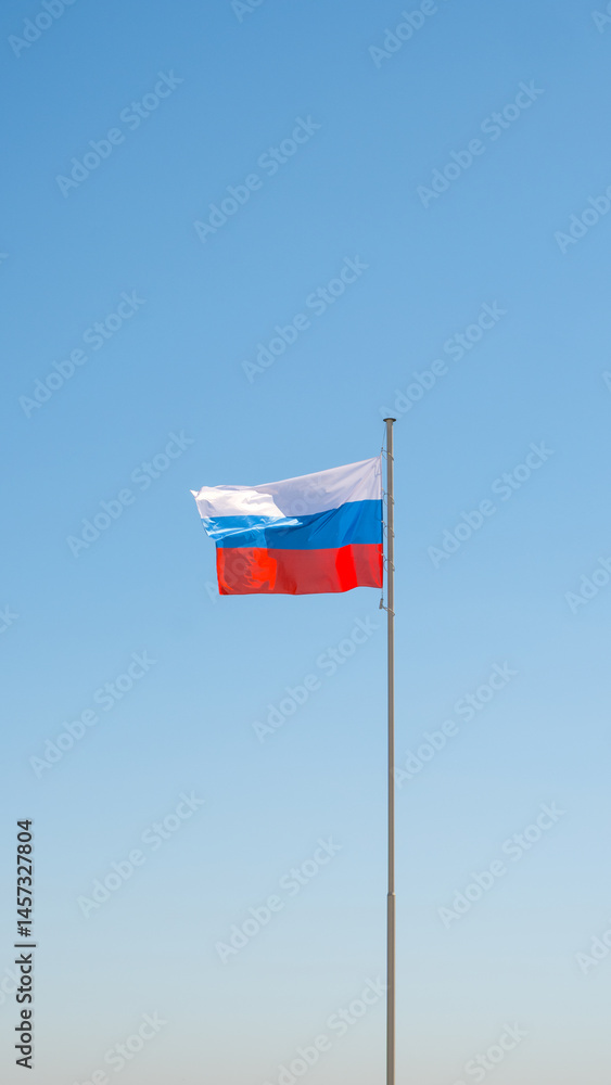 Large flag of the Russian Federation on a flagpole against a blue sky. Close up