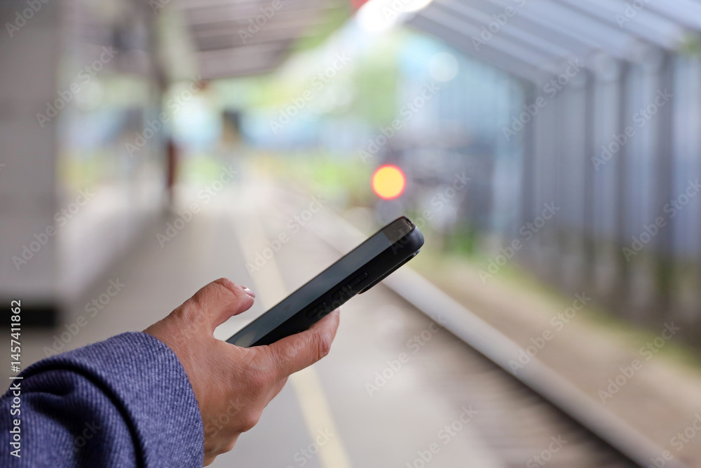 Smartphone in hand of woman waiting for the arriving train on railroad station. Commuter train passenger, online payment for the trip