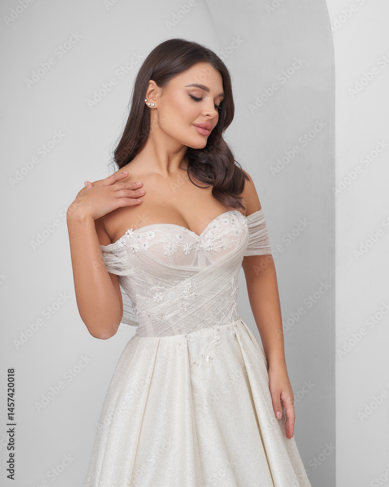 Brunette woman in elegant wedding dress poses in bright interior with graceful arc Brunette woman in elegant wedding dress poses in bright interior with graceful arc