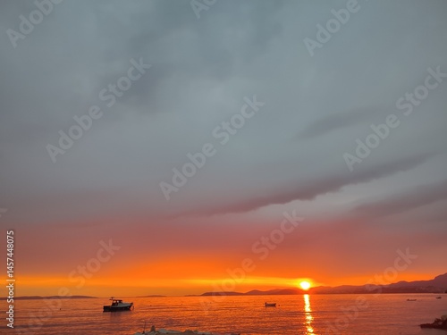 Dramatic Sunset with Stormy Clouds Over Calm Sea and Boats