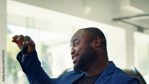 Overjoyed customer in car showroom satisfied with choice after checking features and deciding on best automobile. Cheerful african american man looking at vehicle keys, elated with purchase, camera A