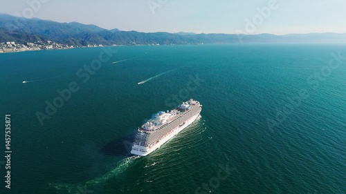 Aerial view of cruise ship sailing away from puerto vallarta, mexico, at sunset, with the city skyline and mountains visible in the distance