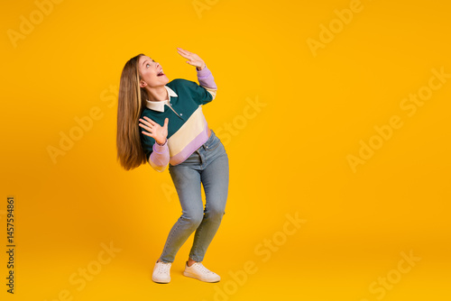 Obraz na płótnie Young woman in casual style gesturing on vibrant yellow background showcasing trendy fashion attire and youthful charm w salonie