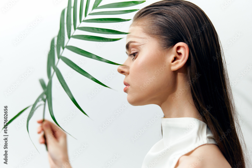 Elegant profile portrait of a woman with long hair and a tropical leaf, showcasing beauty and serenity in a minimalist setting.