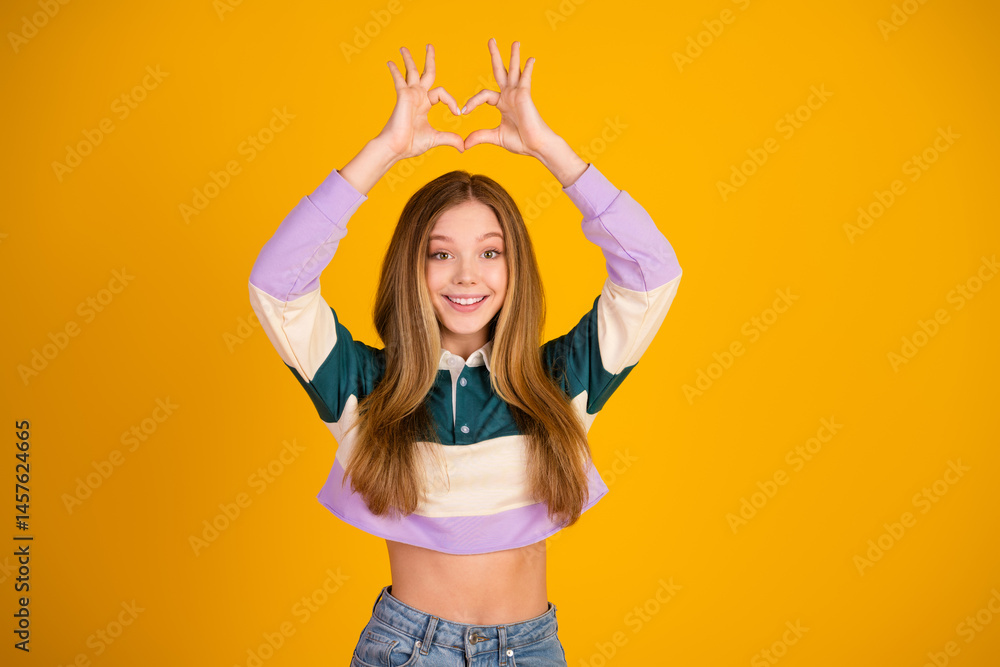 Young lovely woman expressing joy with heart gesture on yellow background