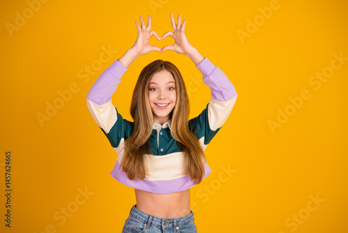 Obraz na płótnie Young lovely woman expressing joy with heart gesture on yellow background w salonie