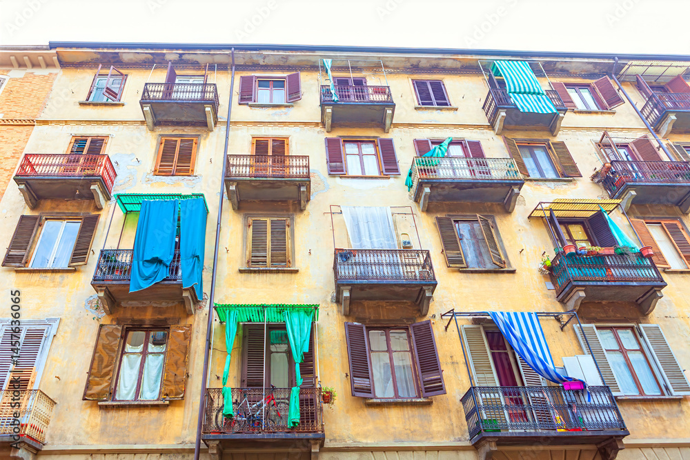 Weathered building with multiple balconies displays a vibrant array of hanging laundry, under a gray sky. Balconies, adorned with plants and bicycles, add a lived-in charm to the urban scene