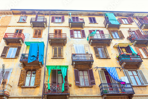 Obraz na płótnie Weathered building with multiple balconies displays a vibrant array of hanging laundry, under a gray sky. Balconies, adorned with plants and bicycles, add a lived-in charm to the urban scene w salonie