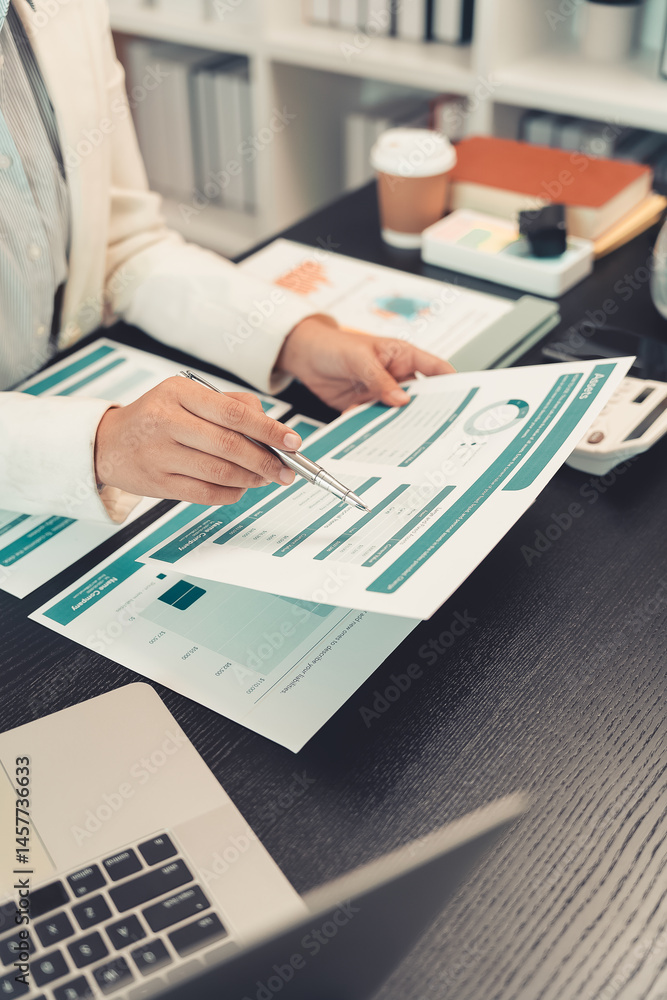 Young female accountant hand holding business investment analysis pen. Accounting, finance expert working with financial data and calculations with graph paper document. Vertical close up.