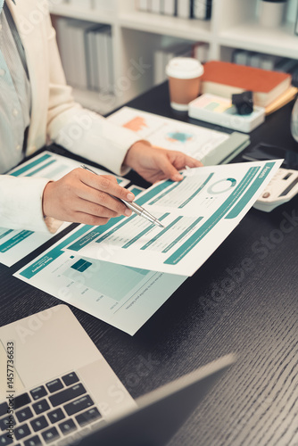 Obraz na płótnie Young female accountant hand holding business investment analysis pen. Accounting, finance expert working with financial data and calculations with graph paper document. Vertical close up. w salonie