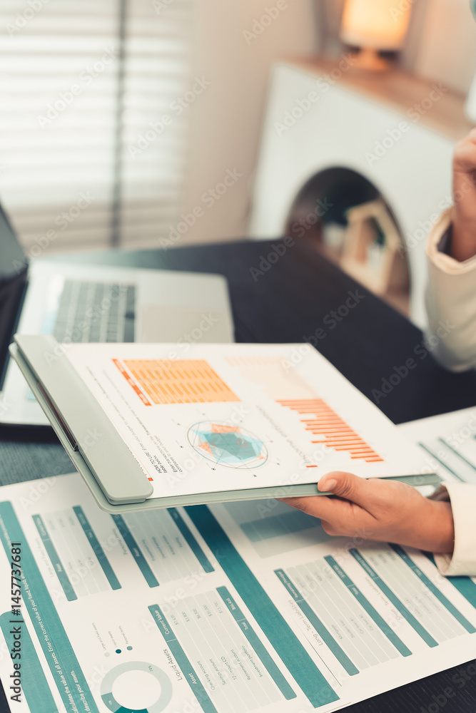 Young female accountant hand holding business investment analysis pen. Accounting, finance expert working with financial data and calculations with graph paper document. Vertical close up.