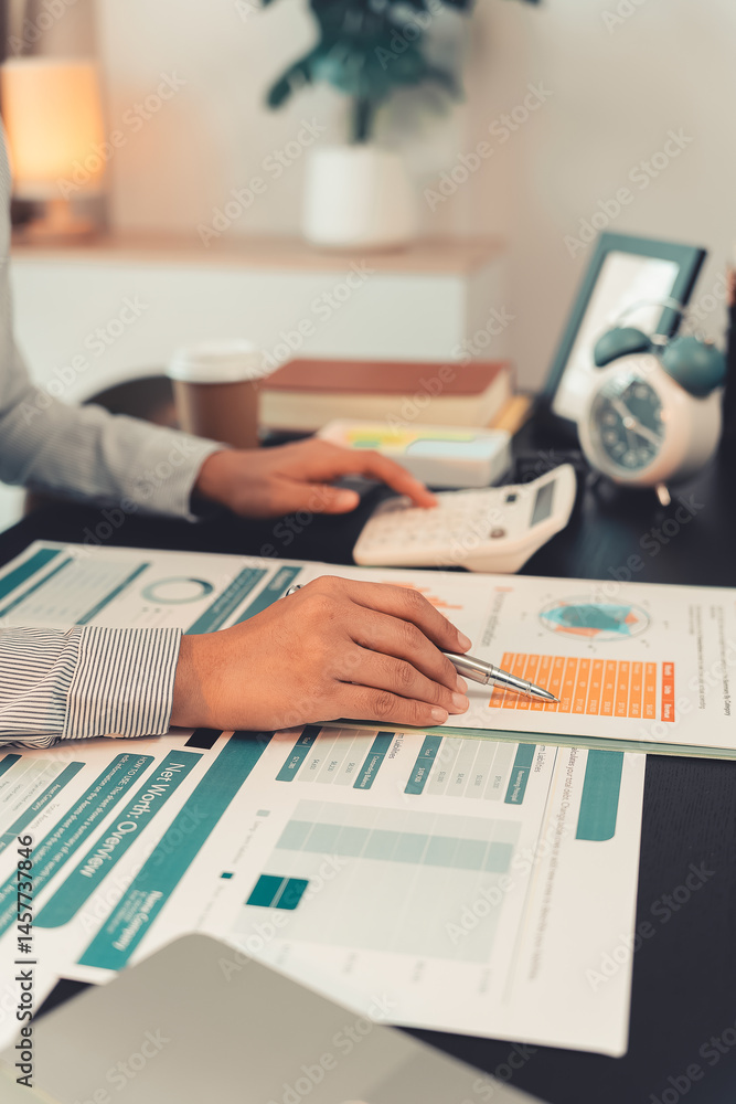 Young female accountant hand holding business investment analysis pen. Accounting, finance expert working with financial data and calculations with graph paper document. Vertical close up.