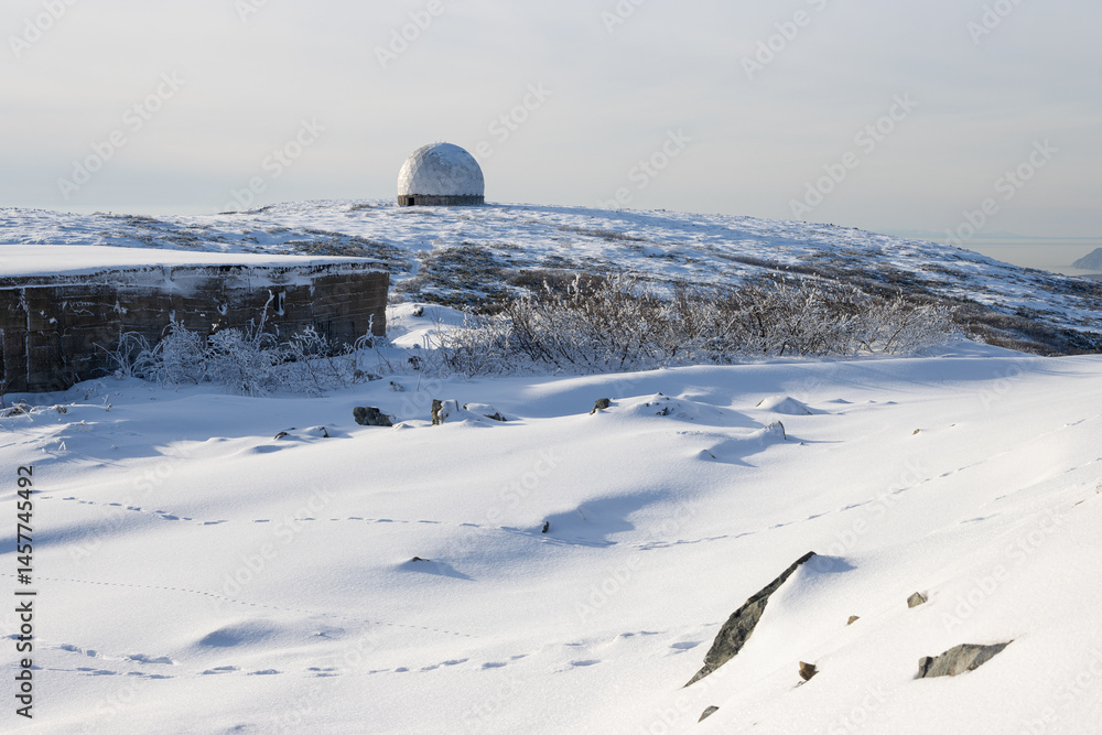 Fototapeta premium The white dome (radiotransparent shelter) of an abandoned radar station on the top of a mountain. Snowy mountain slope. Tourist attraction in the vicinity of Magadan. Magadan region, Far East Russia.