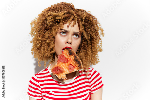 Obraz na płótnie Young woman with curly hair enjoying a slice of pizza, wearing a striped shirt, playful expression, minimalist background showcasing a vibrant and tasty concept w salonie