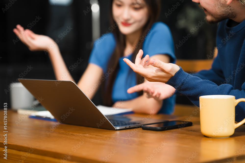 Caucasian man and an Asian woman sit at a table at home, engaged in online learning. They share ideas, talk casually, and sip coffee, creating a relaxed and focused atmosphere Caucasian man and an Asian woman sit at a table at home, engaged in online learning. They share ideas, talk casually, and sip coffee, creating a relaxed and focused atmosphere