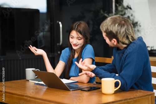 Obraz na płótnie Caucasian man and an Asian woman sit at a table at home, engaged in online learning. They share ideas, talk casually, and sip coffee, creating a relaxed and focused atmosphere w salonie