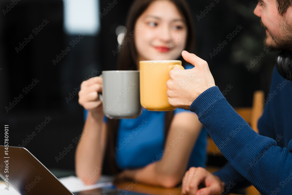 Caucasian man and an Asian woman sit at a table at home, engaged in online learning. They share ideas, talk casually, and sip coffee, creating a relaxed and focused atmosphere