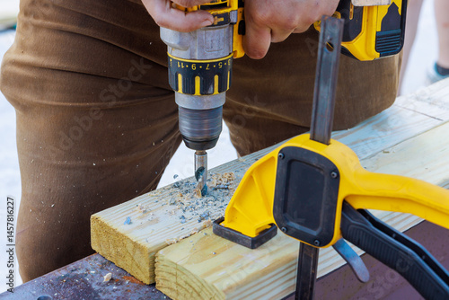 Photography Metalworker uses drill to create holes in wooden planks while working at constru
