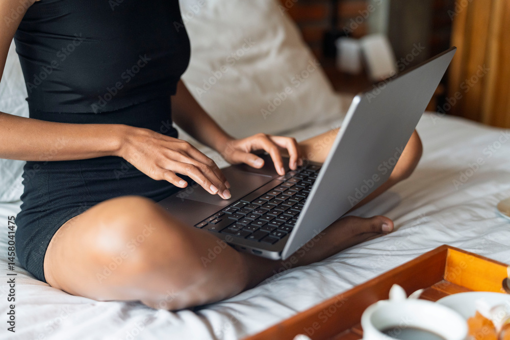 Naklejka premium close-up of women hands using touchpad mouse and keyboard, sitting on the bed working on computer and drink some coffee.