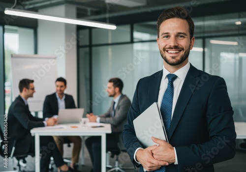 Smiling businessman holding laptop with colleagues in meeting at the office in the background